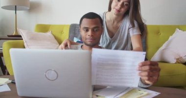Yeni ev sahipleri evrakları birlikte inceliyor. Genç Afrikalı Amerikalı ve Kafkas Milenyum çifti oturma odalarında faturalarını internet üzerinden ödüyorlar. 4k Yavaş çekim el bilgisayarı