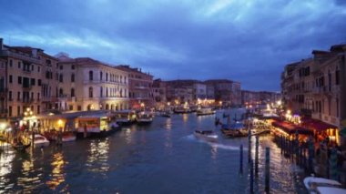 Gece Büyük Kanal ve şehir manzarası üzerinde bulutlu bir akşam gökyüzü. Kanalda seyahat eden teknelerin ve Rialto Köprüsü 'nden gelen renkli Venedik binalarının odaklanmış görüntüsü. 4k