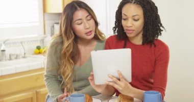 Kahvaltıda tablet bilgisayar kullanan iki kadın arkadaş mutfakta.