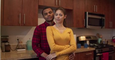 Afrika kökenli Amerikalı erkek ve beyaz kadının portresi. Birbirlerine sarılıp mutfaklarındaki kameraya bakıyorlar. Milenyum çifti evde. 4k ağır çekim el bilgisayarı