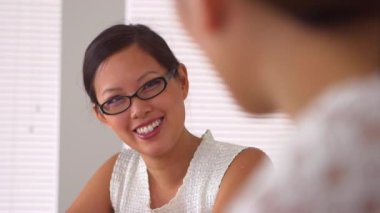 Gülümseyen Çinli kadın iş arkadaşıyla mutlu bir şekilde konuşuyor.