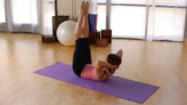 Genç bir kadın paspasın üzerinde pilate hareketi yapıyor.