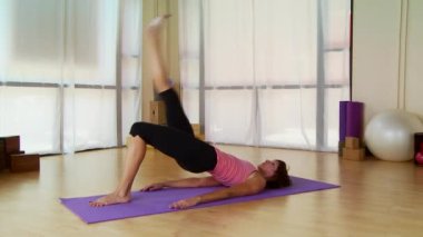 Genç bir kadın paspasın üzerinde pilate hareketi yapıyor.