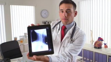 İspanyol doktor boyun röntgenlerini göstermek için tablet ekranı kullanıyor.