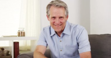 Kanepede gülümseyen kıdemli adam.