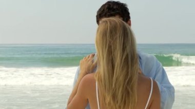 Genç çift okyanusun kenarında öpüşüyor.