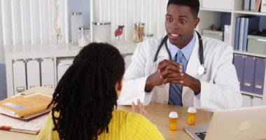 Kadın hasta ofis masasında Afrikalı Amerikalı doktorla konuşuyor.