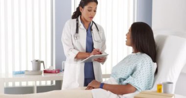 Kadın doktor hastane yatağında Afro-Amerikan hasta konuşuyor