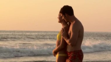 Genç çift gün batımında sahilde öpüşme