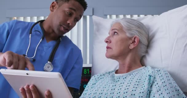 男性の千年黒人看護師は タブレットコンピュータを使用して手術手順のシニア女性の画像を表示します 電子パッドを見ている若いRnと高齢者 — ストック動画