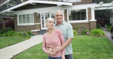 Yeni evin önünde gülümseyen yaşlı bir çift.