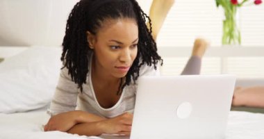 Gülümseyen siyah kadın yatakta dizüstü bilgisayar kullanarak