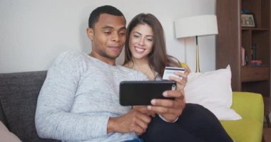 Genç çift, kredi kartı ve akıllı telefonla online alışveriş yapıyor. Milenyum Afrikalı Amerikalı ve Kafkasyalı kadın ve erkek düğün için yer ayırtıyorlar. 4k ağır çekim el bilgisayarı