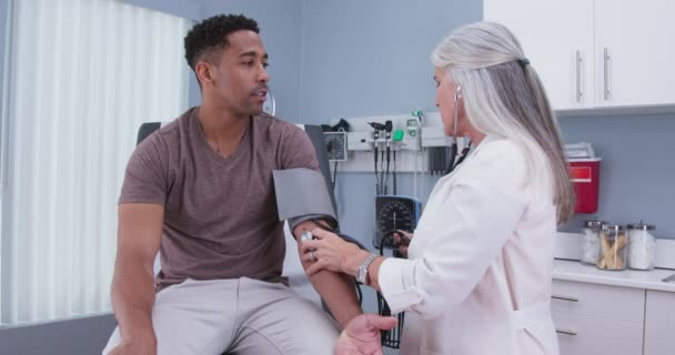 医生抽吸血压计测量男性病人的生命值 与资深女医生进行健康检查的年轻黑人病人测量自己的血压 — 图库视频影像