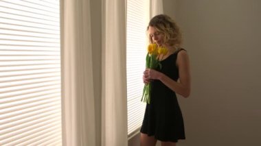 Bir buket lale ile pencerenin yanında duran mutlu sarışın kadın.