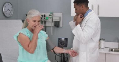 Genç erkek doktor yaşlı kadının tansiyonunu ölçmek için monitör kullanıyor. Yaşlı kadın hastanın tansiyonu genç siyahi hekimler tarafından ölçülüyor.