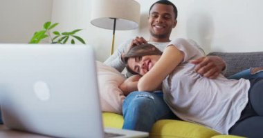 Erkek arkadaşları kanepede yatıp dizüstü bilgisayarlarında film izlerken sevgililerini gıdıklıyor. Siyah ve beyaz çift bir komedi dizisini çevrimiçi yayınlarken gülüyorlar. 4k ağır çekim el bilgisayarı