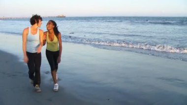 Koşudan sonra deniz kenarında yürüyen iki genç kadın.