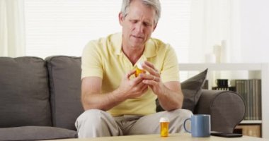 Mutsuz yaşlı adam ilaç şişelerini tutuyor.