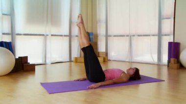 Genç bir kadın paspasın üzerinde pilate hareketi yapıyor.