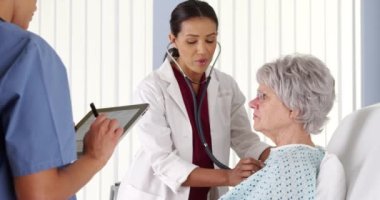 Afro-Amerikalı doktor, olgun bir hastanın nefes alışını steteskopla dinliyor.