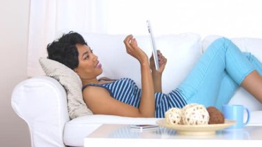 Oturma odasında tablet bilgisayarını kullanan siyah bir kadın.