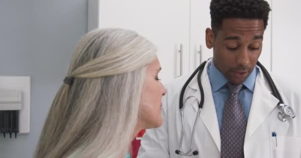 オフィスの中で成熟した白人女性と話す千年の黒人医師の終わり 室内で健康クリニックを議論する医師と患者のタイトなショット — ストック動画