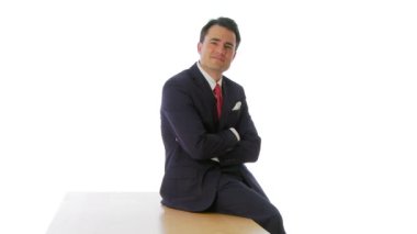 İş adamı masaya oturmuş kameraya gülümsüyor.