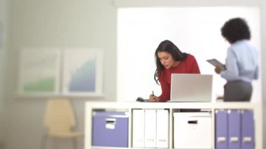 Laptop 'ta arka planda iş arkadaşlarıyla çalışan İspanyol iş kadını.