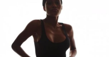 Afrikalı kadın kameraya bakıyor ve beyaz arka planda dans ediyor.