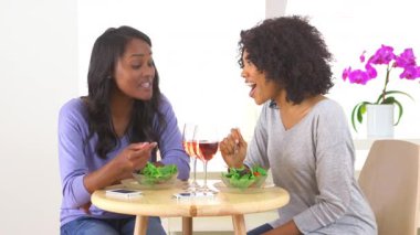 İki Afrikalı Amerikalı kadın birlikte gülüyor ve salata yiyor.