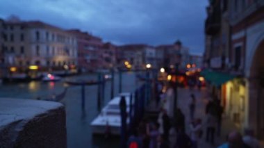 Şehir ışıklarıyla Büyük Kanal 'da gece yürüyüşü ve tekne trafiği. Gondollar gri bulutlu gökyüzünün altında süzülürken turistler kanalın yanından geçiyorlar. 4k