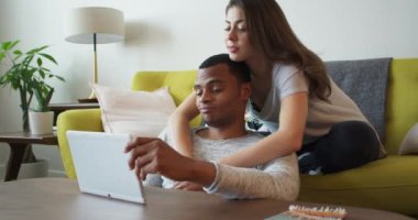 Tablet bilgisayarına bakarken kollarını erkek arkadaşının omzuna koyan mutlu genç bir kadın. Afrika kökenli Amerikalı ve Kafkasyalı çiftler mobil cihaz kullanarak seyahat etmeyi planlıyorlar. 4k Yavaş çekim el bilgisayarı