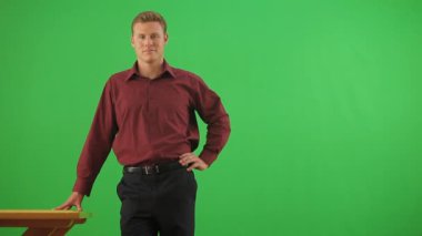 İş adamı masaya yaslanmış kameraya bakıyor.