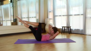 Genç bir kadın paspasın üzerinde pilate hareketi yapıyor.