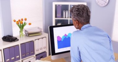 Siyahi kıdemli iş kadını bilgisayardaki çizelgeleri analiz ediyor.