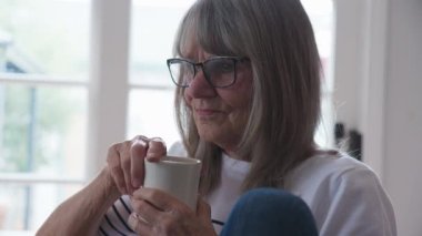 Çalışırken bir fincan kahve içen son sınıf beyaz kadın. Elinde bir kupa çay tutan yaşlı bir kadının arka ışıklandırması. Yavaş çekim 4k