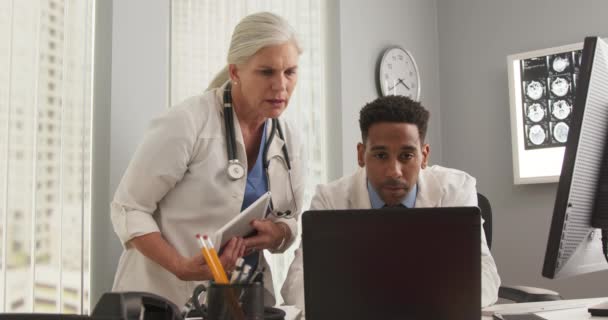 2人の医師がオフィスで働き ラップトップコンピュータを使用しています ノートパソコンの仕事をしている若い黒人医師で先輩の同僚に相談しながら — ストック動画
