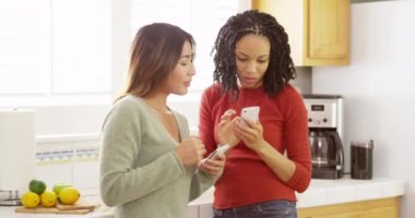 İki yakın arkadaş cep telefonunu kullanarak ve mutfak tezgahı karşı yaslanmış