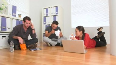 Meksikalı ve beyaz çalışanlar ofis zemininde yemek yiyorlar.