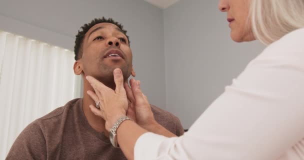 成熟的女医生检查男性病人颈部是否有肿大的甲状腺或淋巴结 高级医生检查病人颈部室内诊所 — 图库视频影像
