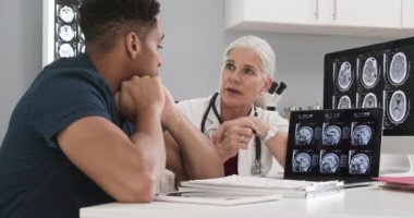 Genç siyah erkek hasta beyin sarsıntısı geçirdikten sonra beyin tomografisine bakıyor. Başhekim hastanın röntgenlerini göstermek için dizüstü bilgisayar kullanıyor.