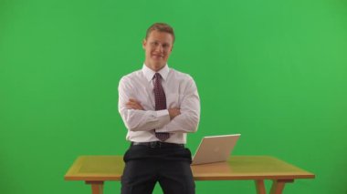 İş adamı masanın kenarında oturuyor, kameraya bakıyor.