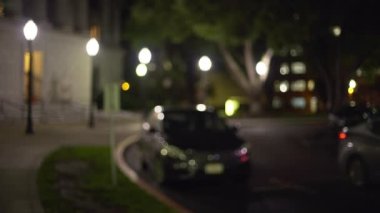 Gece yarısı sakin bir sokakta park halindeki arabaların kamera arkası görüntüsü. Eyalet Kongre Binası 'ndan geçen bir araba. 4k