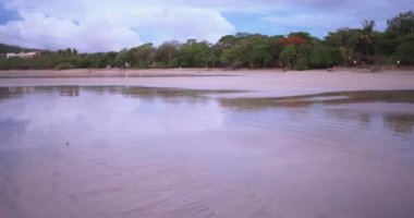 Kosta Rika 'da tropikal plajda ıslak kumu kapatın. Yağmur ormanı ağaçlarının plaja yansıyan odaksız görüntüsü. 4k