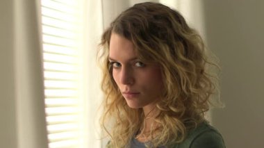 Sarışın, kıvırcık saçlı kadın pencerede bekliyor.