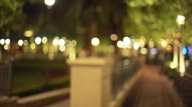 Gece vakti boş park yolunun arka planında odaklanmış plaka yok. Ağaçları ve bokeh ışıkları olan güzel şehir parkının video arkaplanı. 4k