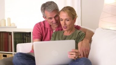 Kocasının gözlerini laptoptan kapayan bir eş.