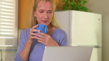 Yetişkin bir kadın bilgisayar kullanırken sabah kahvesini içiyor.
