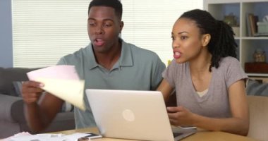 Hüsrana uğramış genç siyahi çift dizüstü bilgisayarla finans ve faturaları tartışıyor.